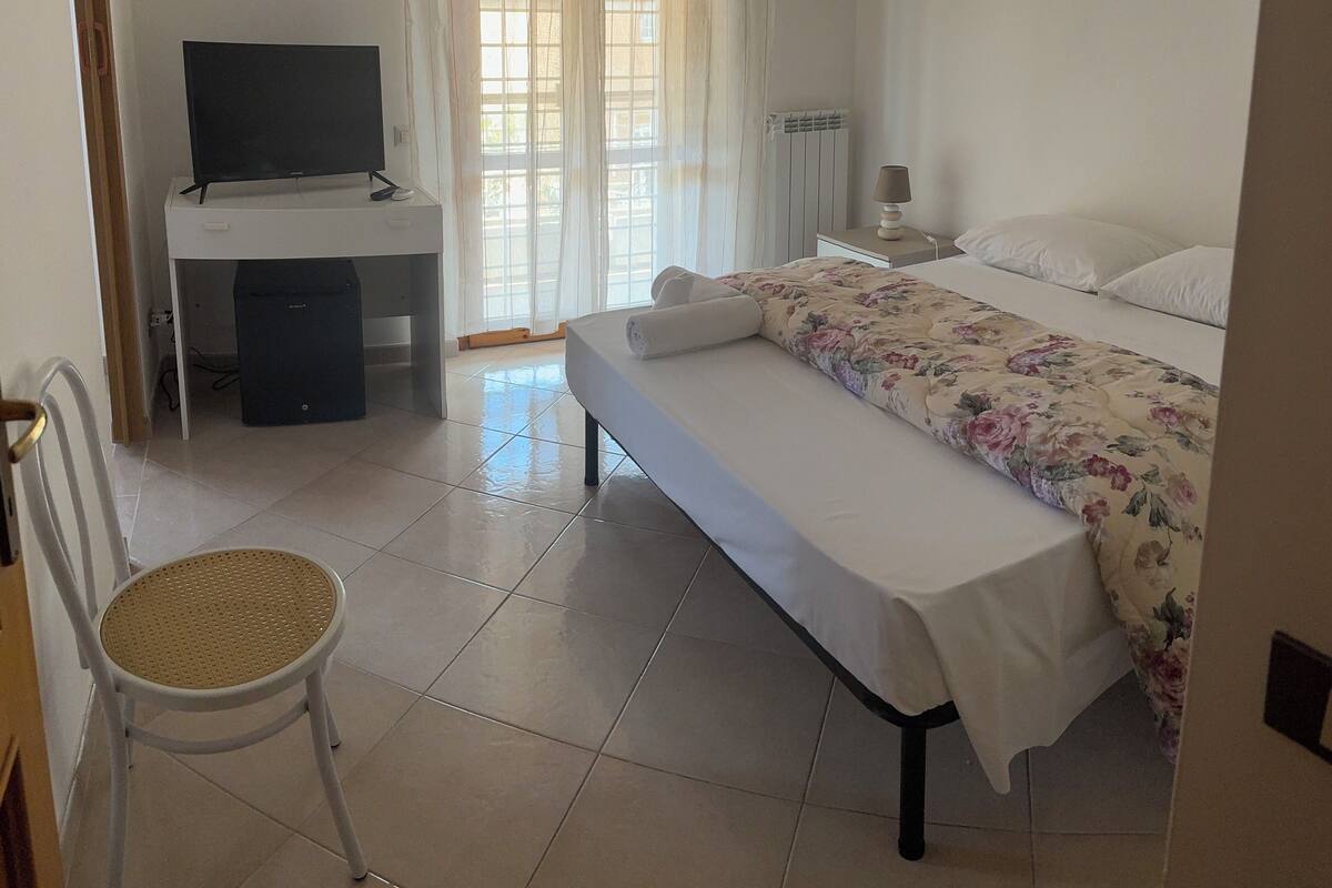 A hotel room with a bed, a desk with a television, a chair, and a window with curtains.