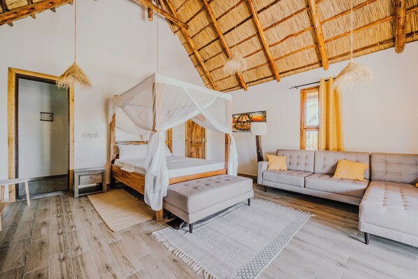 A bedroom with a four-poster bed, a sofa, and a wooden floor. - Zaria Garden Bungalow (Pwani Mchangani)