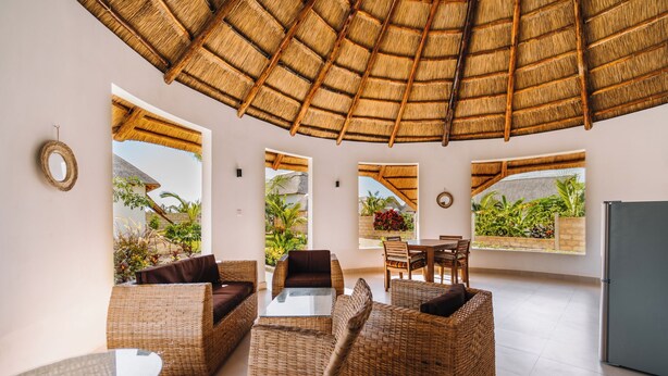 A spacious room with wicker furniture, large windows, and a thatched roof. - Zaria Garden Bungalow (Pwani Mchangani)