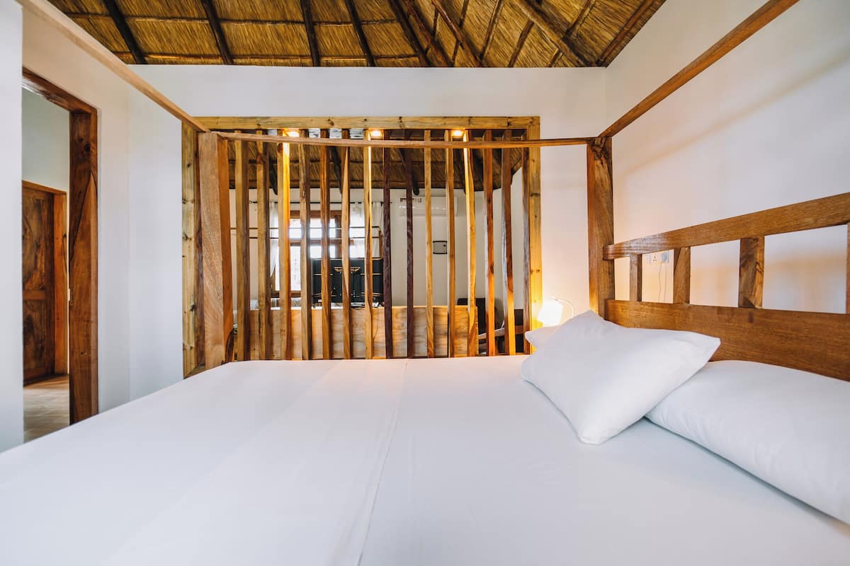 Una habitació amb un llit, un capçal de llit de fusta i un sostre de palla.