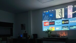 Une chambre à coucher comprenant un lit, un bureau et un écran fixé au mur, sur lequel sont affichés différents services de diffusion en continu.