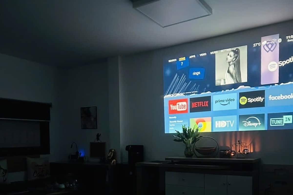 A bedroom with a bed, a desk, and a wall-mounted screen displaying various streaming services.