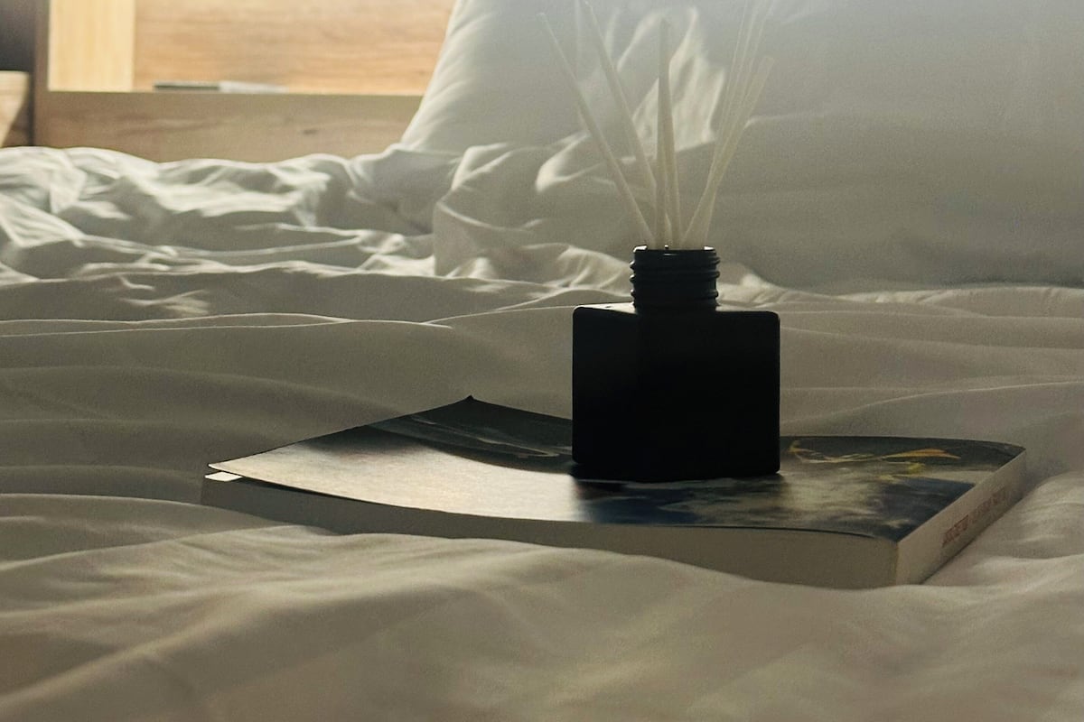 A bed with a book and a black object on it, a wooden headboard, and a wall with bookshelves.