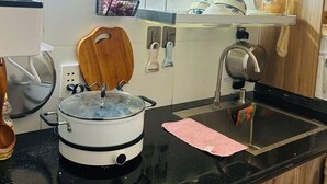 Une cuisine compacte équipée d’un four à micro-ondes, d’une mijoteuse et d’une bouilloire. On y trouve des ustensiles en bois et un étendoir suspendu pour la vaisselle.
