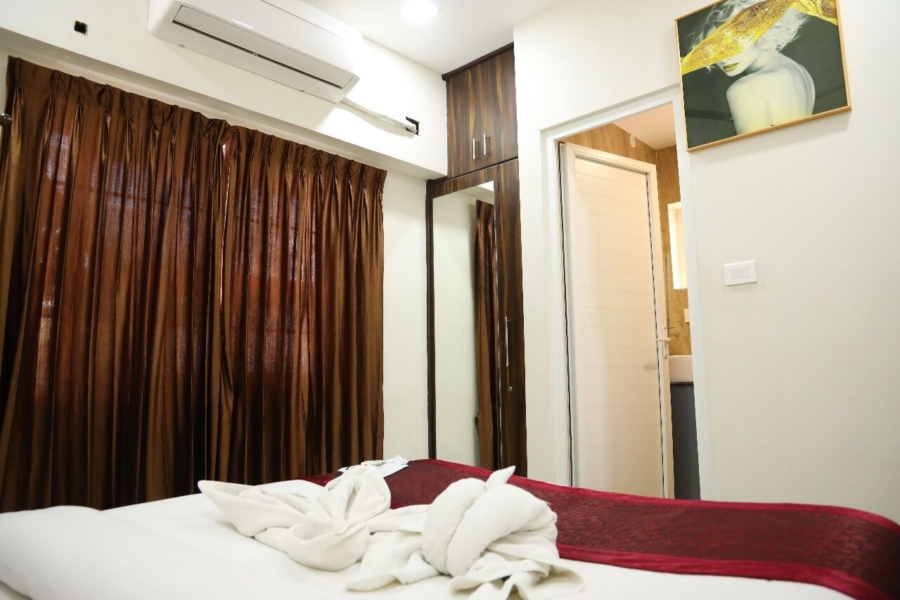 A hotel room with a bed, a red blanket, a white towel, a brown curtain, a mirror, and a painting on the wall.