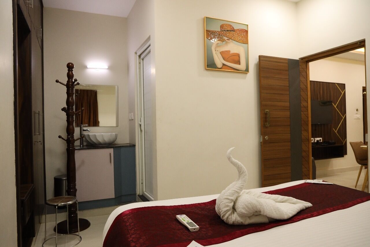 Una habitación de hotel con una cama, un perchero de madera, un baño con un lavabo y un cuadro en la pared.