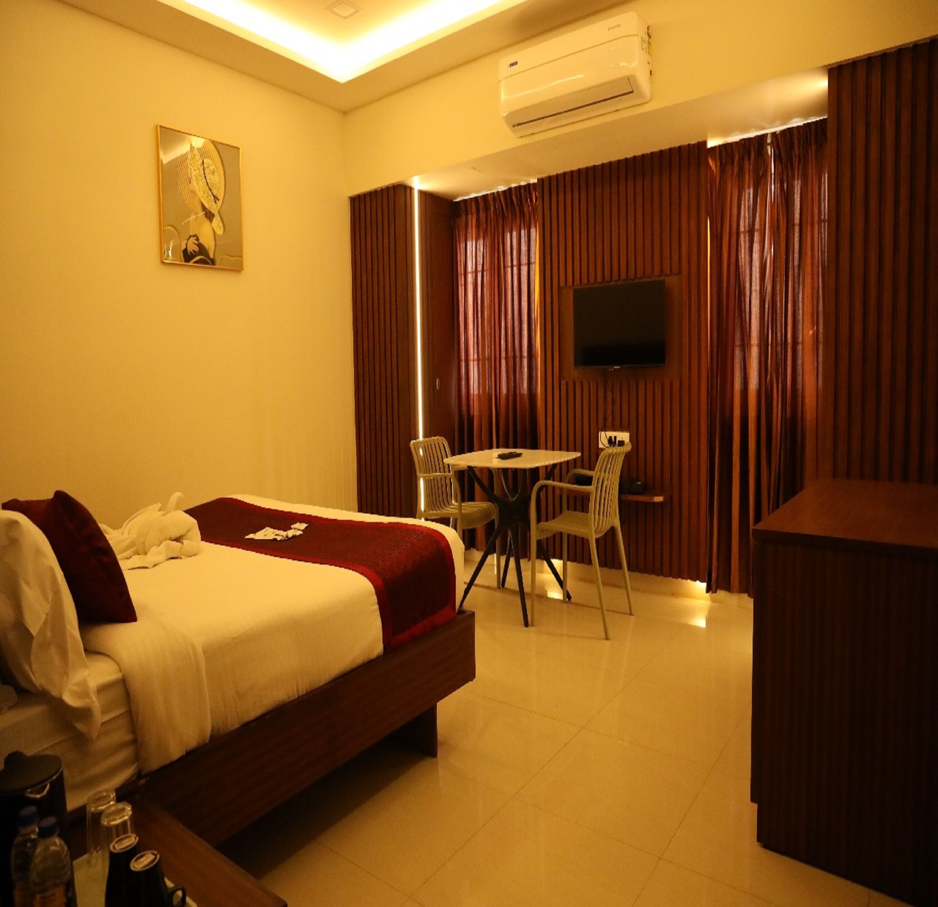 A hotel room with a bed, a desk, a chair, a television, and an air conditioning unit.