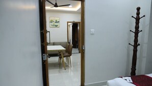 A bedroom with a bed, a wooden headboard, a dining area with a table and chairs, and a ceiling fan. - Manopriya Residency by Azalea (Madurai)