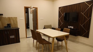 A modern kitchen with a marble countertop, a coffee maker, and a dining area with a white table and brown chairs. - Manopriya Residency by Azalea (Madurai)