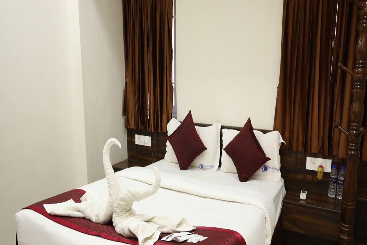 A neatly made bed with a white comforter and red accents, a wooden headboard, and a wooden nightstand with a lamp.