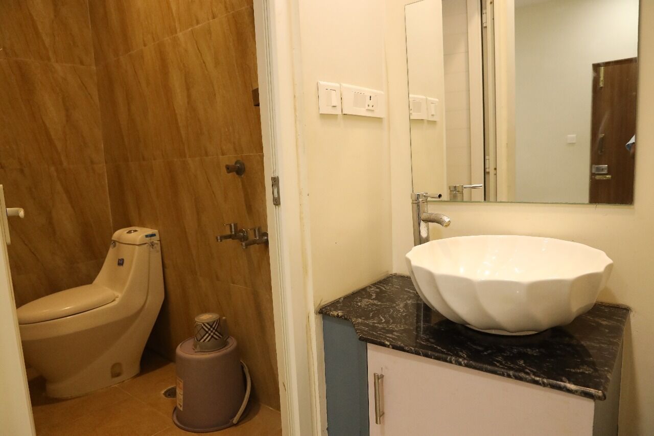 Une salle de bain équipée de toilettes, d’un lavabo, d’un miroir et d’une poubelle.