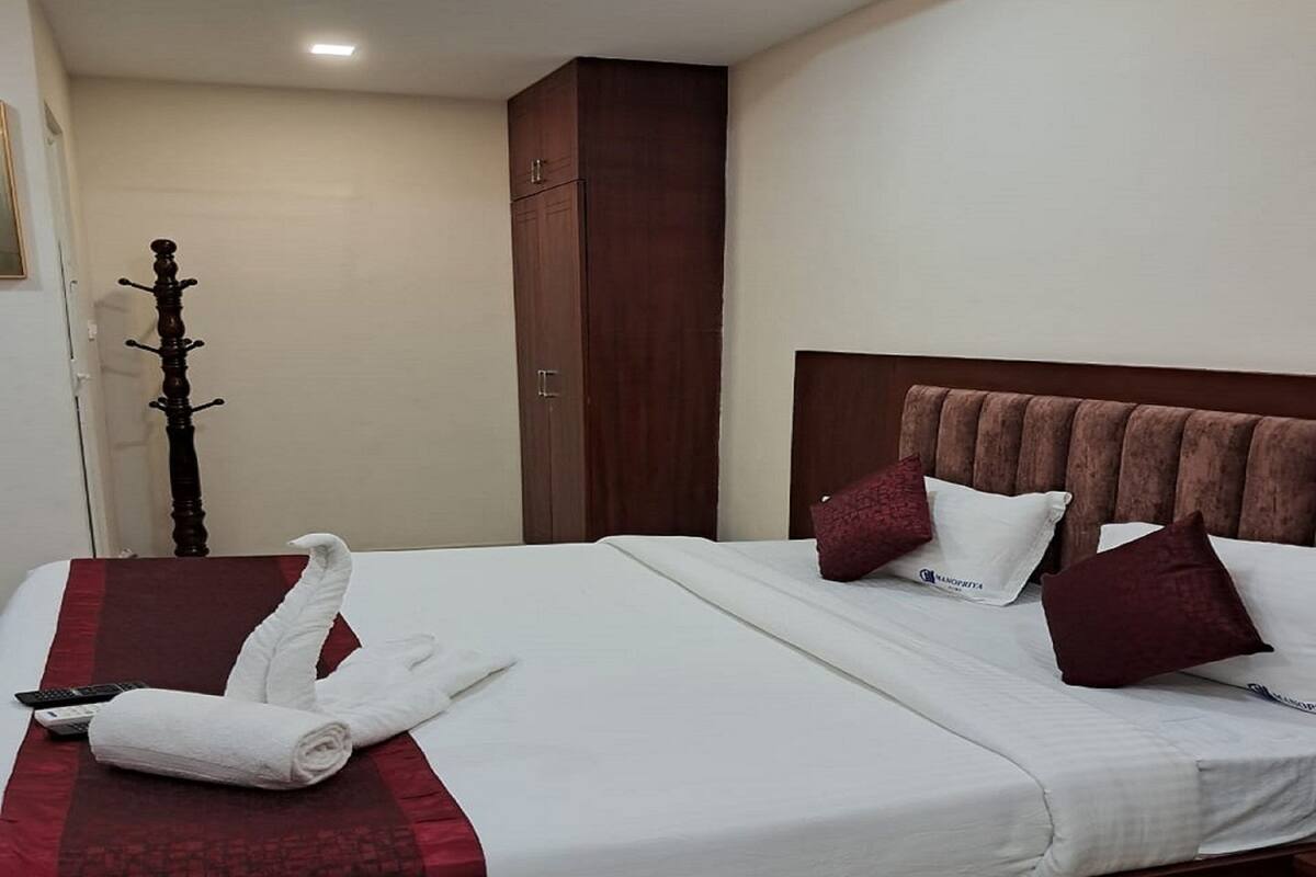 A hotel room with a neatly made bed, a wooden wardrobe, and a coat rack.