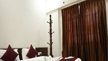 Une chambre d’hôtel avec un lit, un poteau de lit en bois, un plaid rouge et des rideaux marron.
