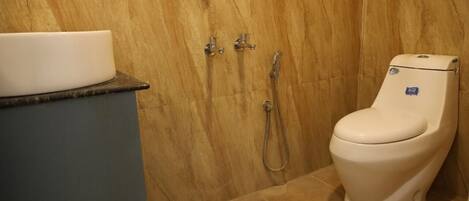 Un baño con inodoro blanco, lavabo y ducha con cabezal de ducha manual.