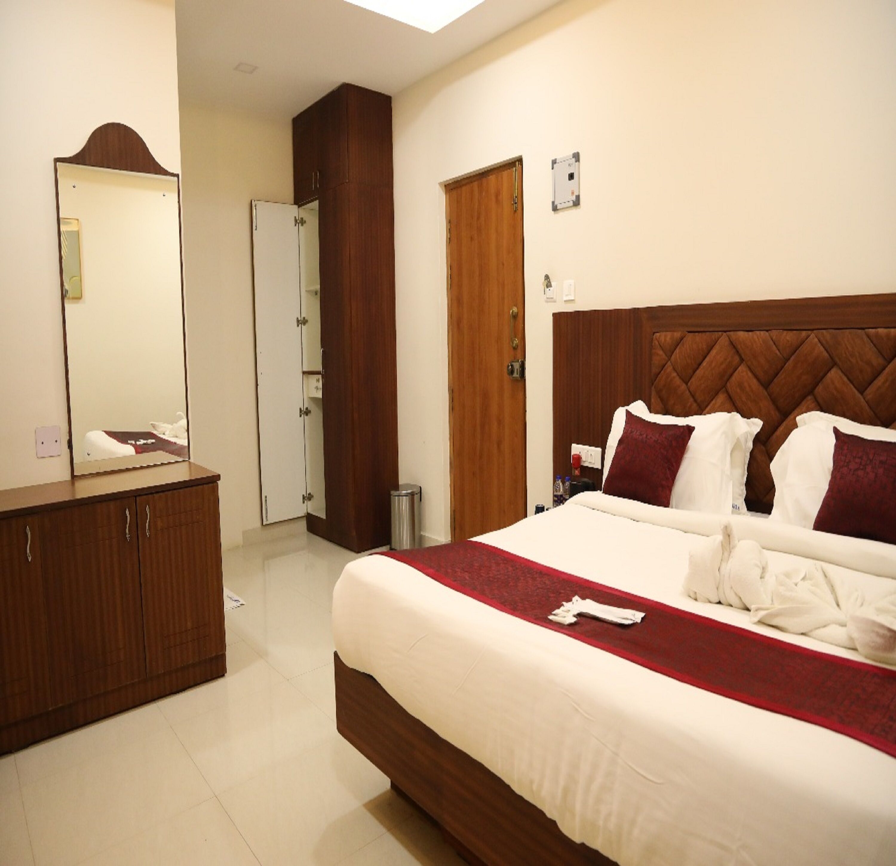 Habitación de hotel con cama grande, cabecera de madera, un espejo, un armario y una puerta.