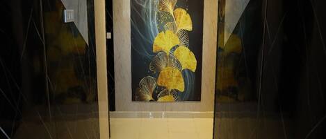 A hallway with a tiled floor and walls, leading to a door with a framed artwork of yellow flowers.