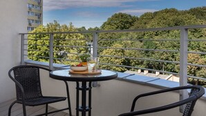 A balcony with a round table and two wicker chairs, overlooking a forested area.