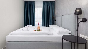 A modern hotel room with a neatly made bed, a bedside table, and a lamp.