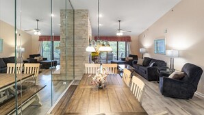 Ein geräumiges Wohnzimmer mit einem Holzespeisetisch, dunklen Sofas und einer Glastrennwand.