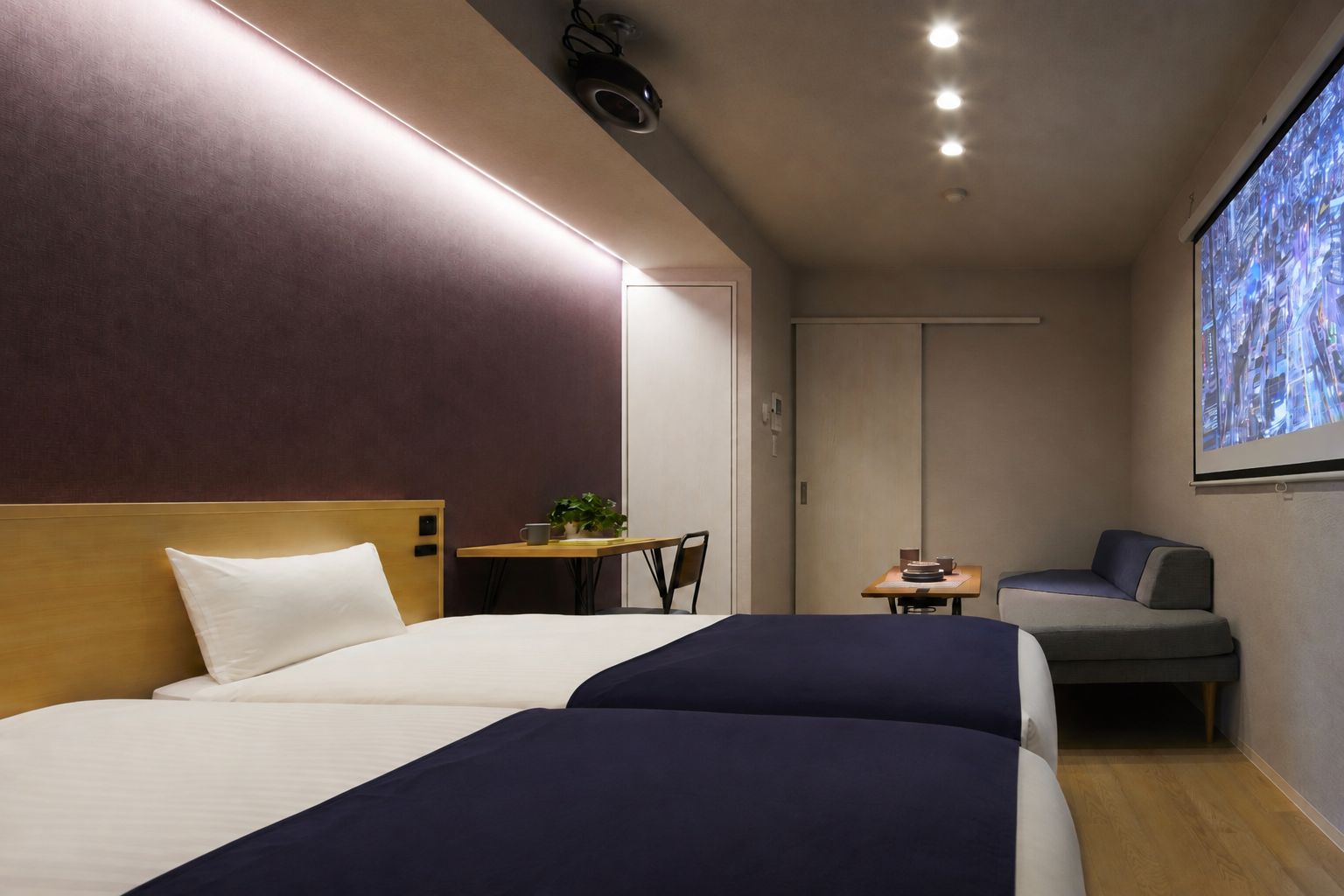 Une chambre d’hôtel avec deux lits, un bureau, une chaise, un canapé et un grand écran diffusant une vue sur la ville.