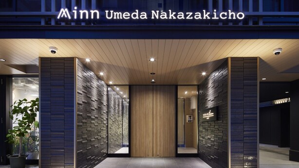 The entrance to a hotel with a modern design, featuring a wooden panel ceiling and a sign above the entrance.