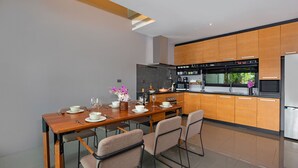 A modern kitchen with wooden cabinets, a dining table with chairs, and a built-in oven. - Designer 4BR Pool Villa Gentle Breeze (Kamala)
