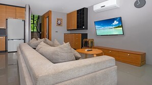 A modern living room with a sofa, a TV, and a wooden cabinet. - Designer 4BR Pool Villa Gentle Breeze (Kamala)