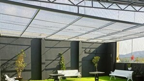 Uma área externa coberta com grama sintética, bancos e plantas em vasos.