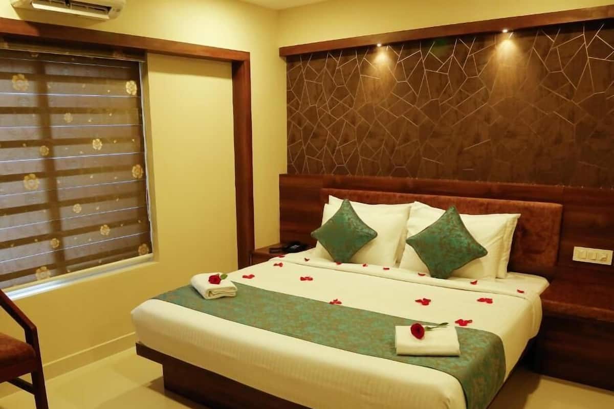 A neatly made bed with a green and white bedspread, two green pillows, and a folded towel with a rose on it.