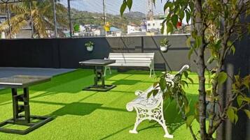 Un patio al aire libre con césped artificial, una mesa, un banco y plantas en macetas.