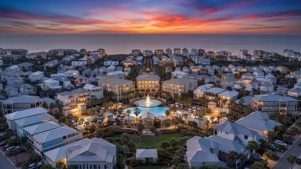 Un complejo turístico con piscina central, varias edificaciones y vistas al atardecer.