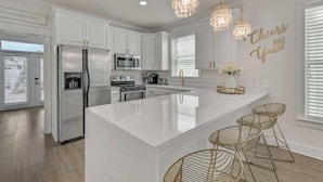 Una cocina moderna con muebles blancos, electrodomésticos de acero inoxidable, una isla grande y sillas de metal.