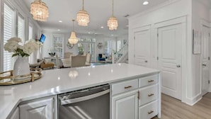 Una cocina amplia con una isla blanca, luces colgantes y armarios blancos.