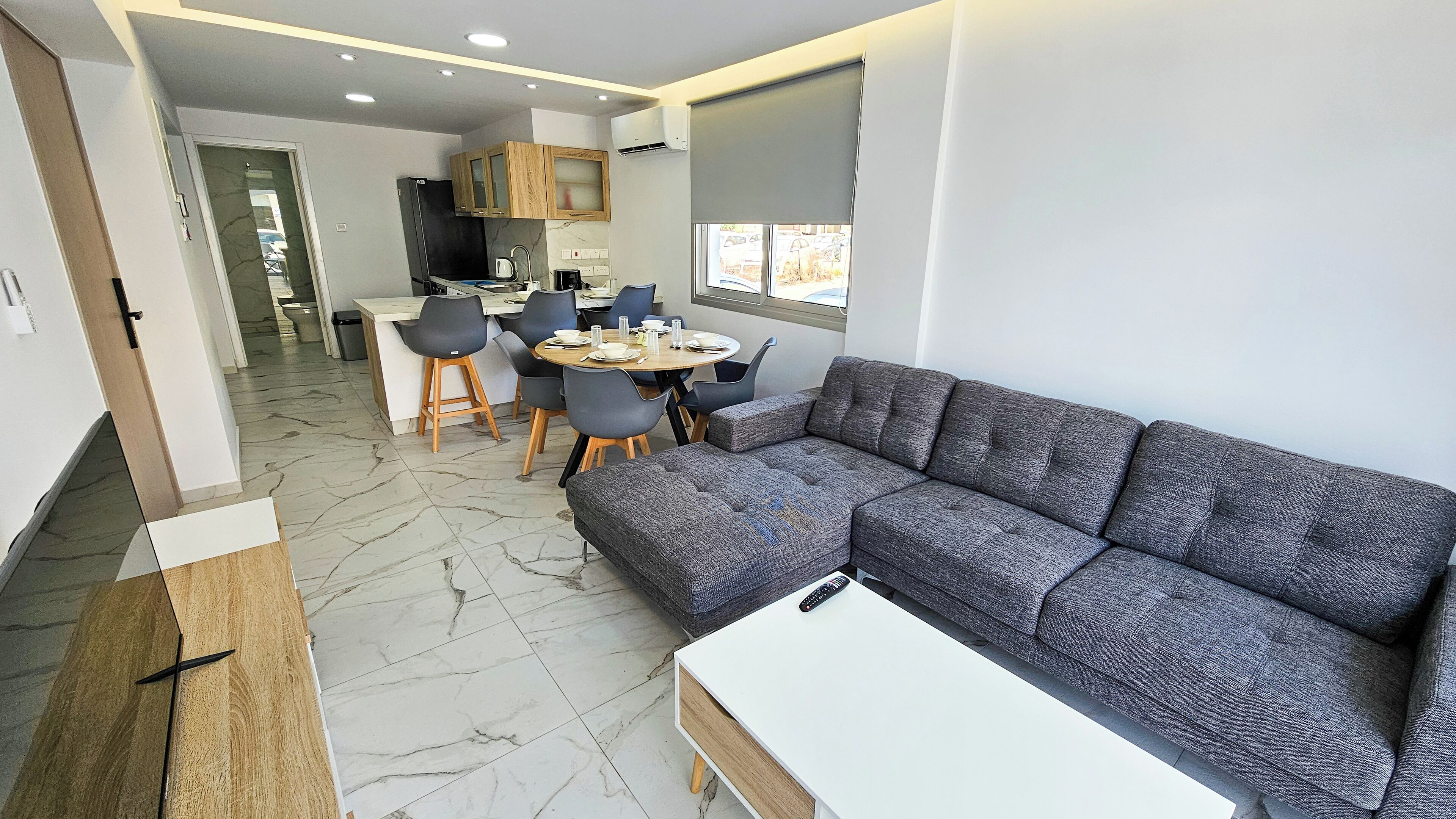 A modern living room with a grey sectional sofa, a white coffee table, and a dining area with a round table and chairs.