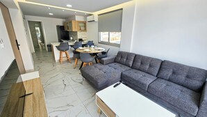 A modern living room with a grey sectional sofa, a white coffee table, and a dining area with a round table and chairs.