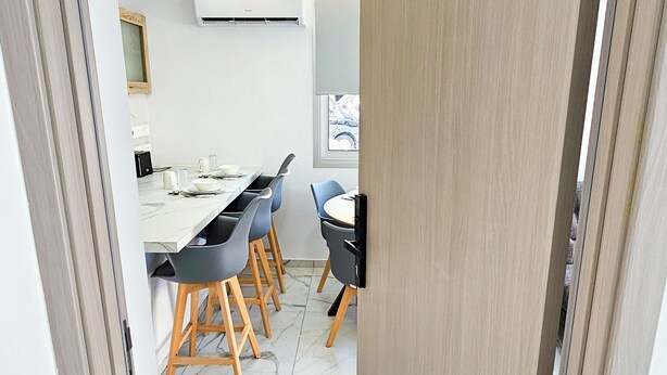 A modern interior with a marble floor, a wooden door with a number, and a dining area with chairs and a table.