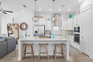 A modern kitchen with white cabinetry, a central island with stools, stainless steel appliances, and pendant lighting. - Resort Pool | 3 Bikes |Golf Cart Included | 30A (Walton County)