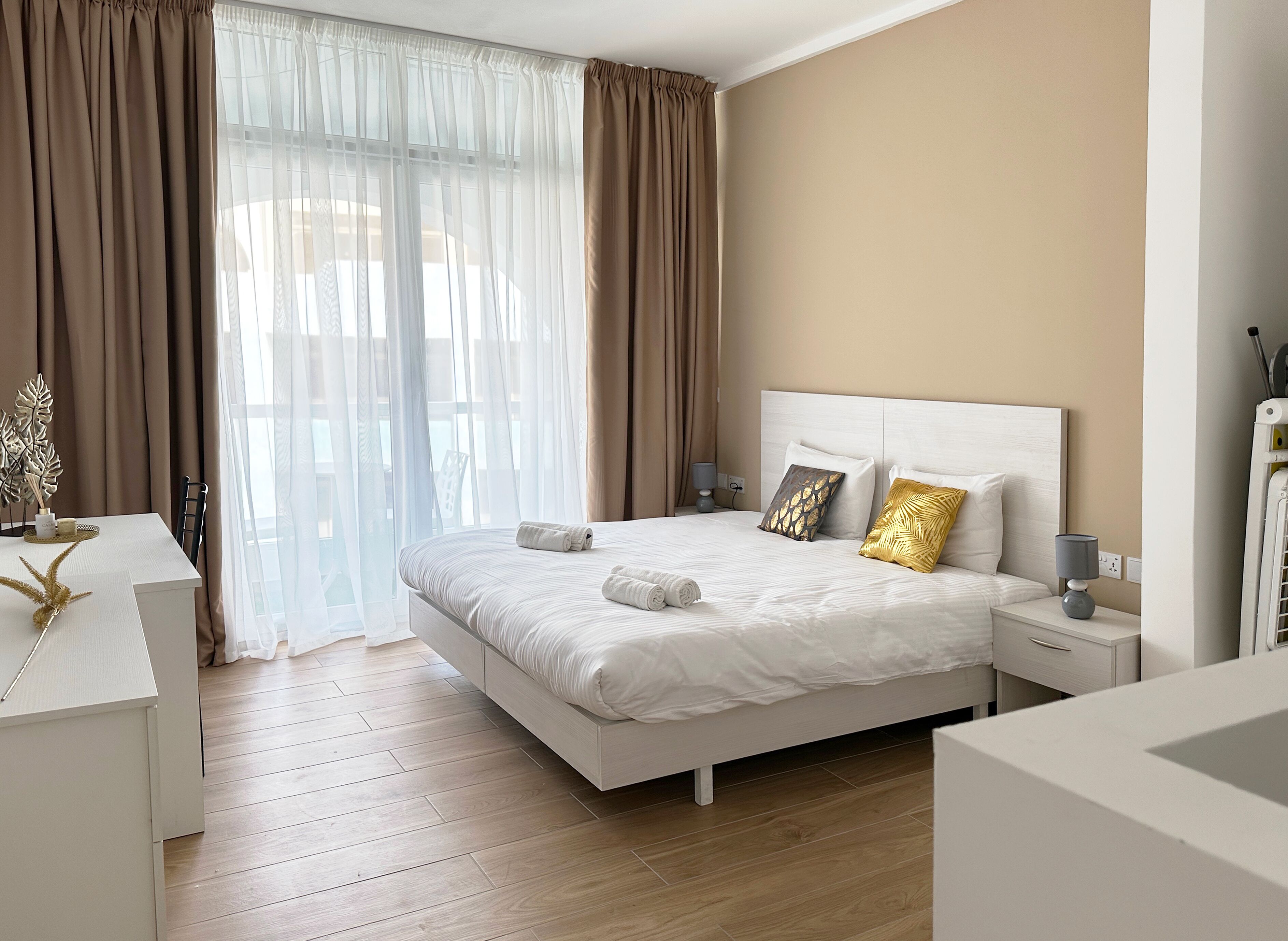 Habitació d'hotel moderna amb un llit gran, taules de nit, escriptori i vista a través de cortines primes.