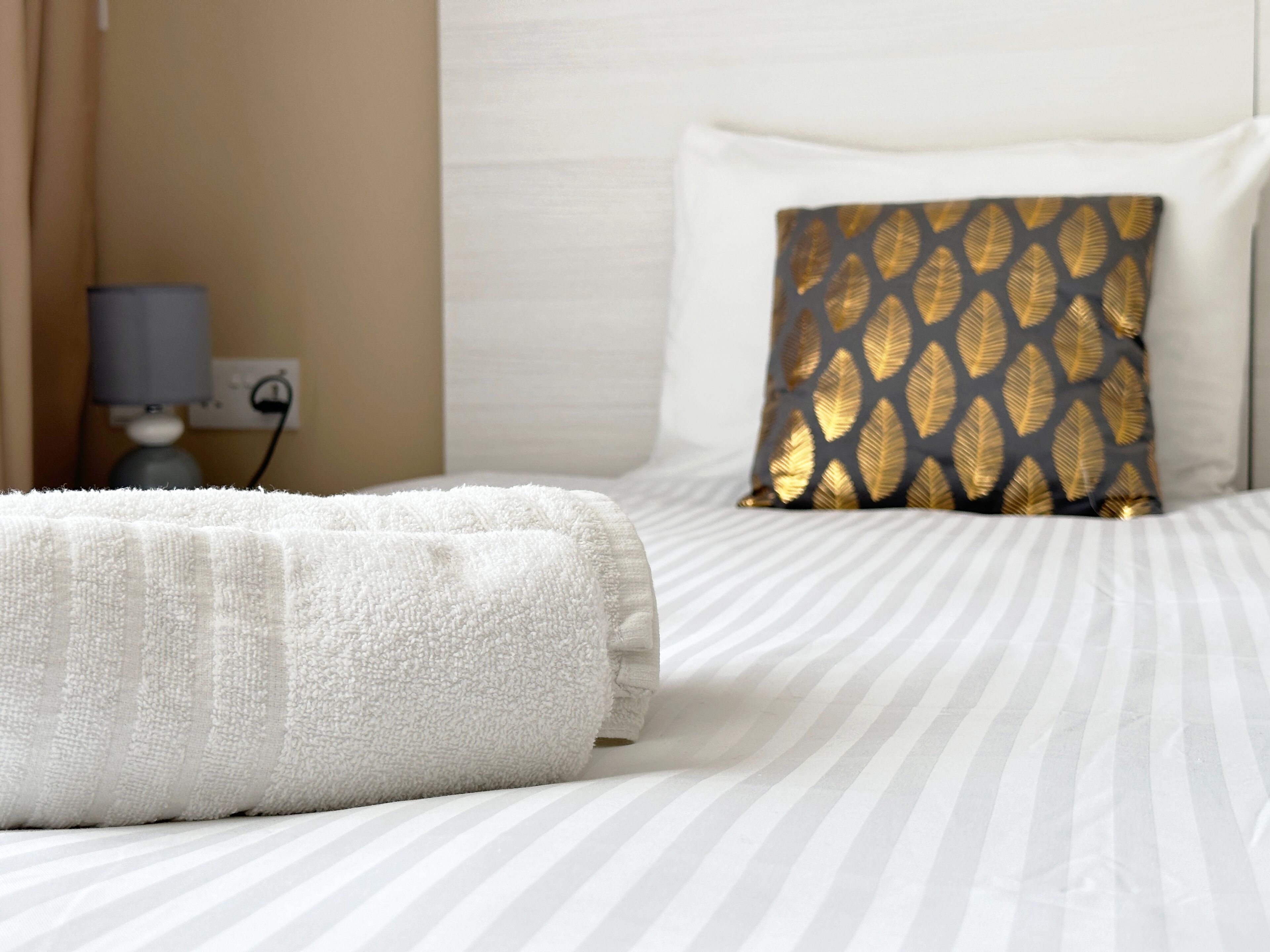 A neatly made bed with a white towel and a patterned pillow.