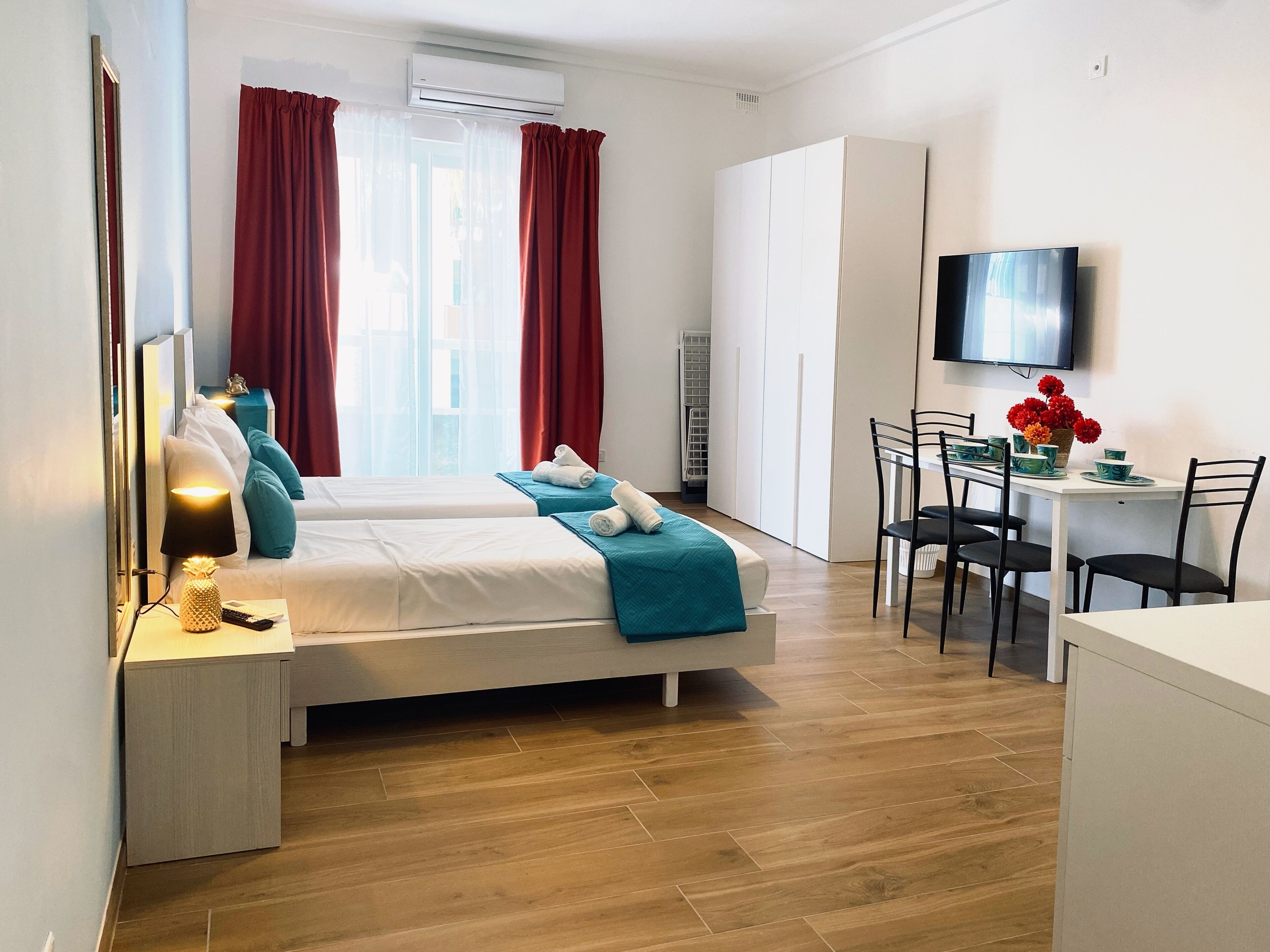 A hotel room with two beds, a desk with chairs, a TV, and a window with curtains.