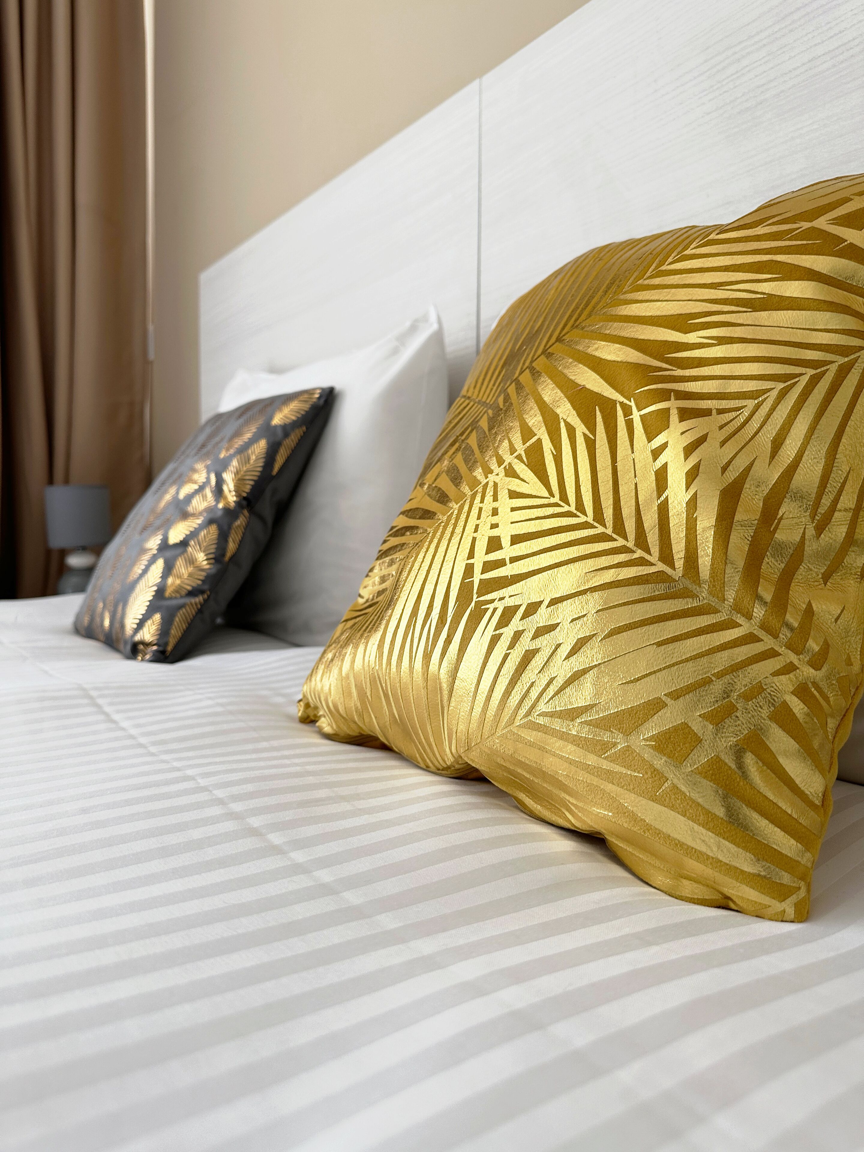 Una cama con una colcha a rayas y dos almohadas, una con estampado de hojas y la otra con diseño geométrico.