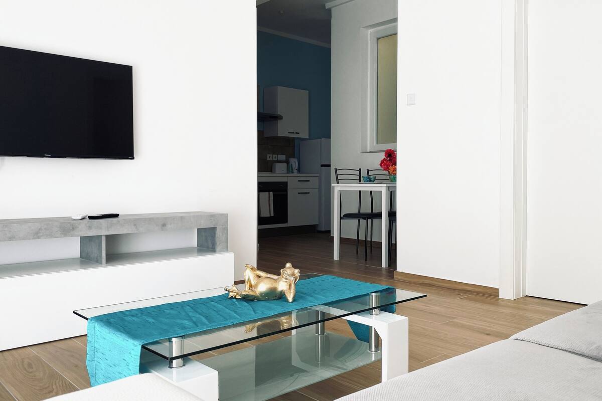 A modern living room with a glass coffee table, a sofa, and a TV mounted on the wall.