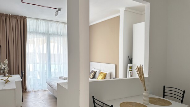 A modern hotel room with a bed, a dining table with chairs, a mirror, and a view of the outside. - Miami Apartments (St. Julian's)