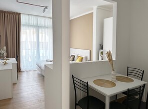 Una habitación de hotel moderna con una cama, una mesa de comedor con sillas, un espejo y vistas al exterior.