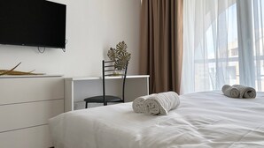 A hotel room with a bed, a desk, a chair, a television, and a window with curtains. - Miami Apartments (St. Julian's)