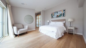 Un dormitorio moderno con una cama grande, un sofá, una mesita de noche, una lámpara, un espejo y un cuadro en la pared.