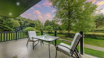 A covered patio with a table and chairs, overlooking a well-maintained garden and a body of water.