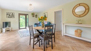 Un coin repas avec une table ronde, des chaises, un vase rempli de tournesols et un téléviseur en arrière-plan.