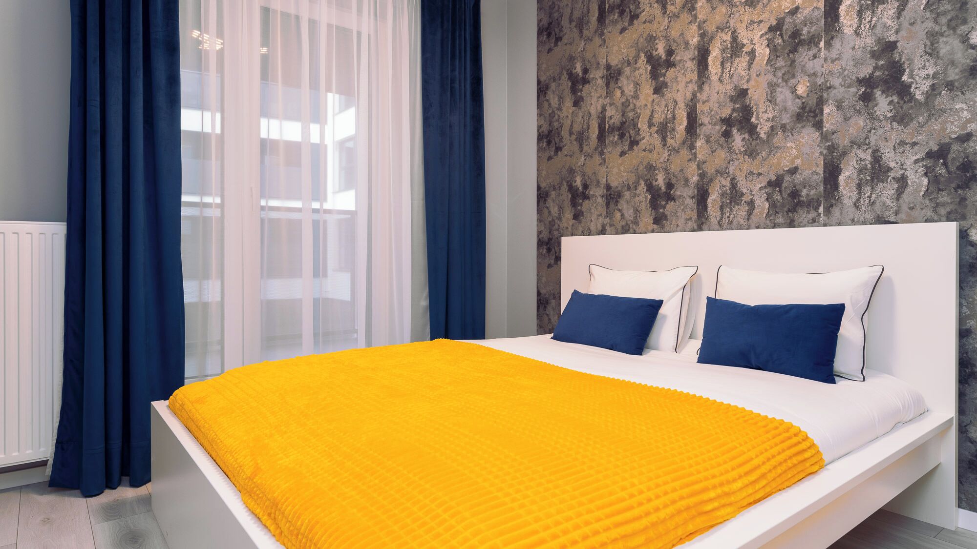 A modern bedroom with a white bed, two blue pillows, and a yellow throw blanket.