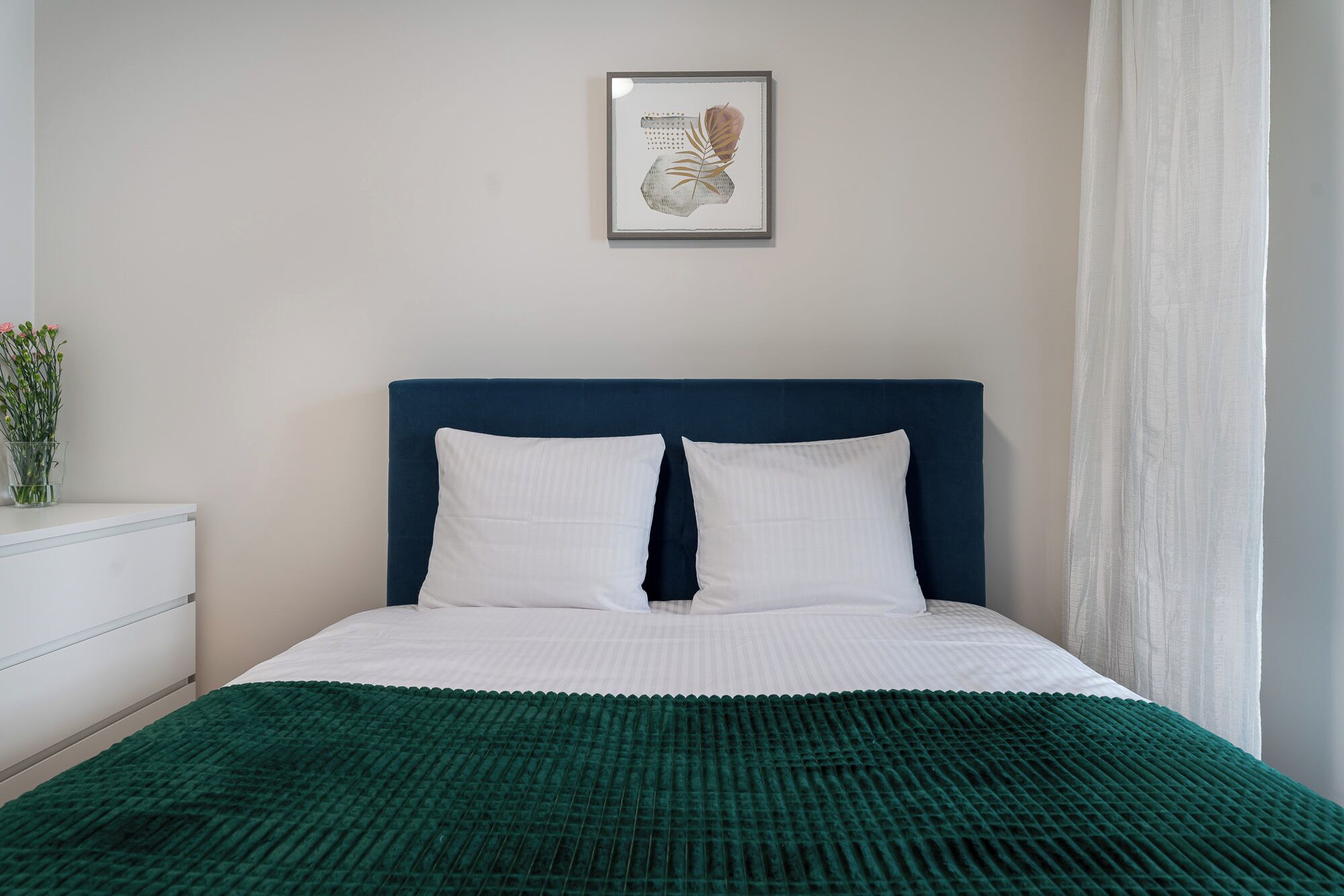 Ein ordentlich bezogenes Bett mit dunklem Kopfteil, weißen Kissen und einer grün gemusterten Decke.